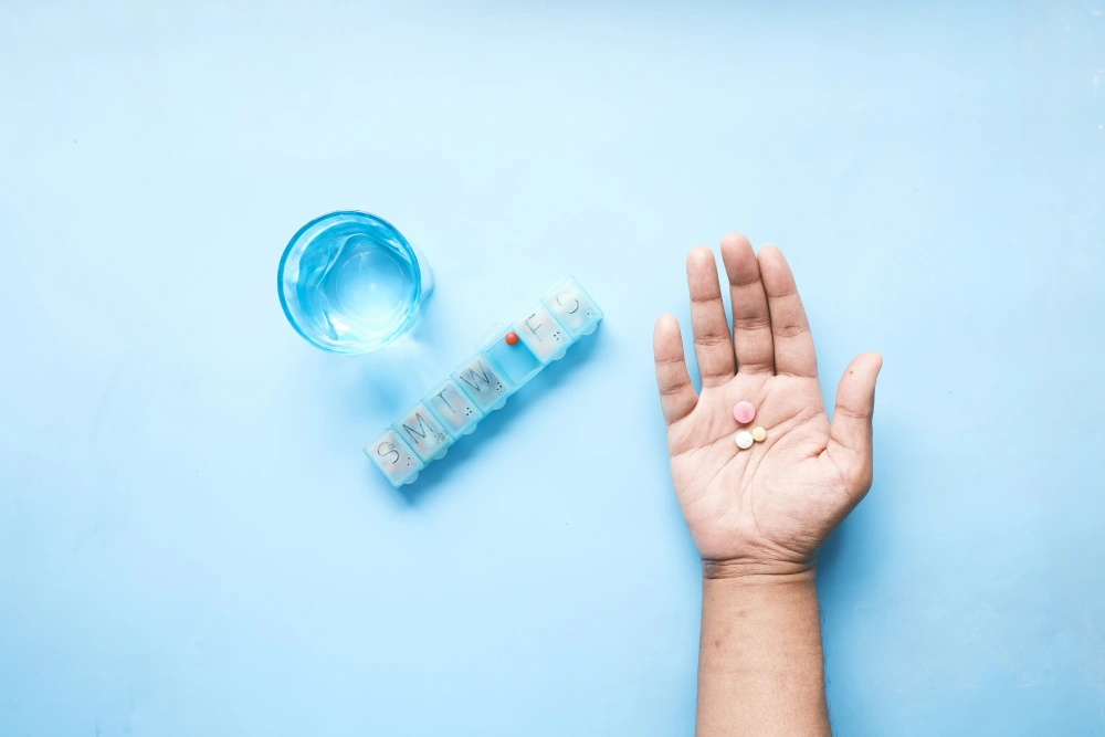 Person holding medication with a weekly pill organizer nearby